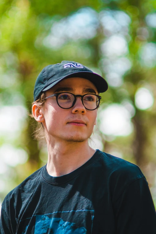 a man wearing glasses standing in front of trees