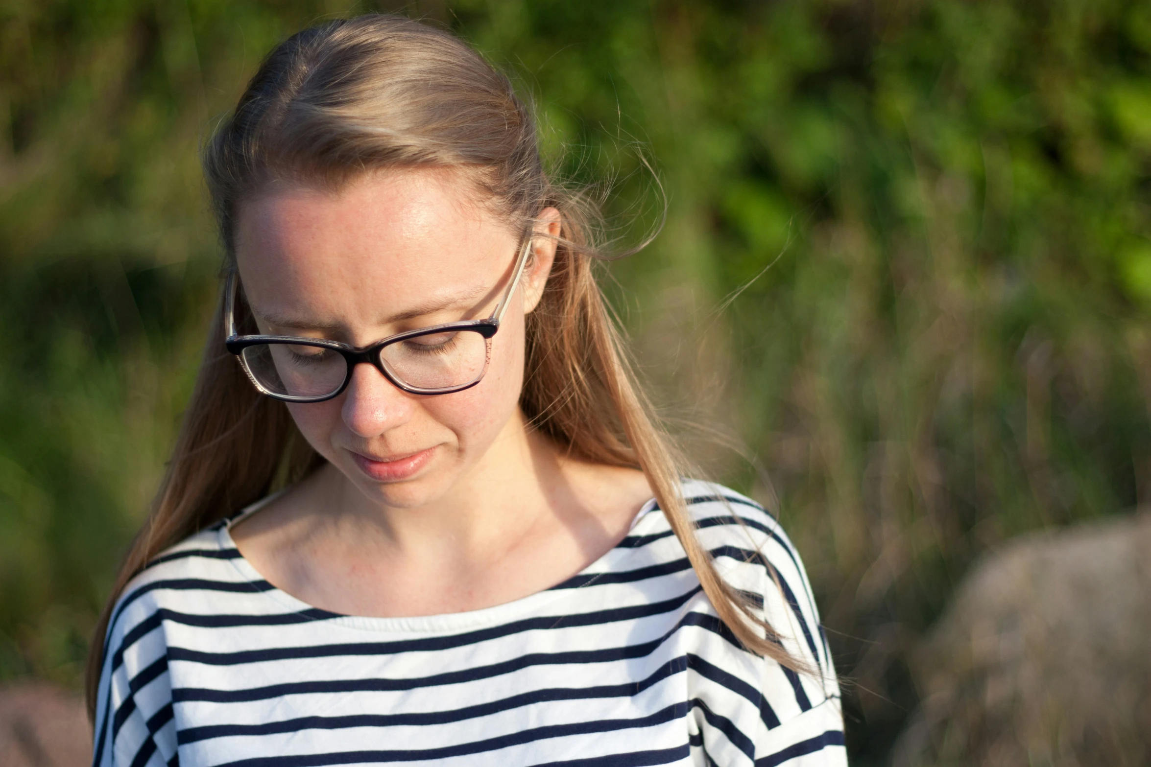 a girl wearing glasses looking down while holding her cell phone