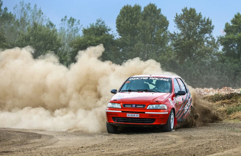 a small red car driving down a dirt road