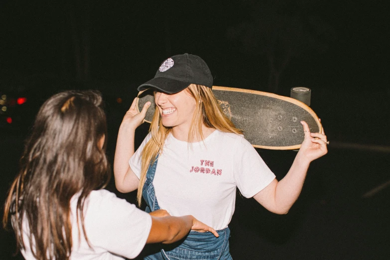 a girl in overalls holding a skateboard behind her back