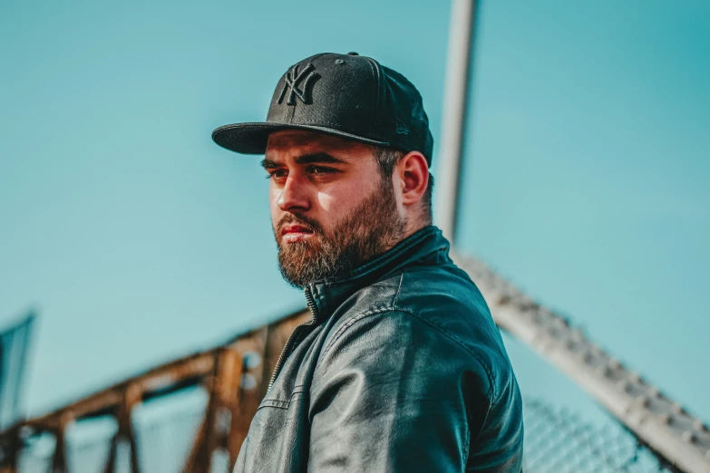 a man wearing a baseball hat stands in front of a chain link fence