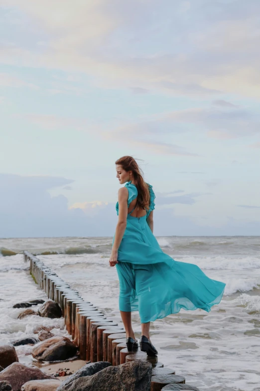 a woman in blue dress standing on a pier next to a large body of water