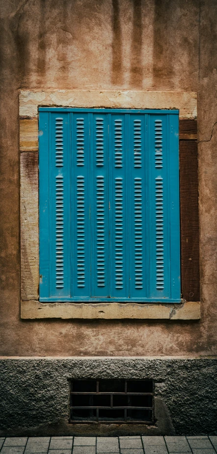 a blue shuttered window with cobblestone floor below