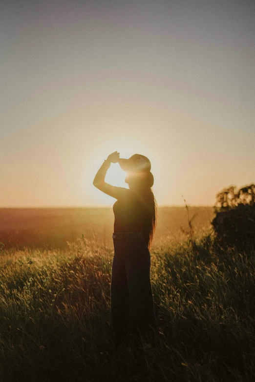 the sun is rising over a women who is standing on a grassy area