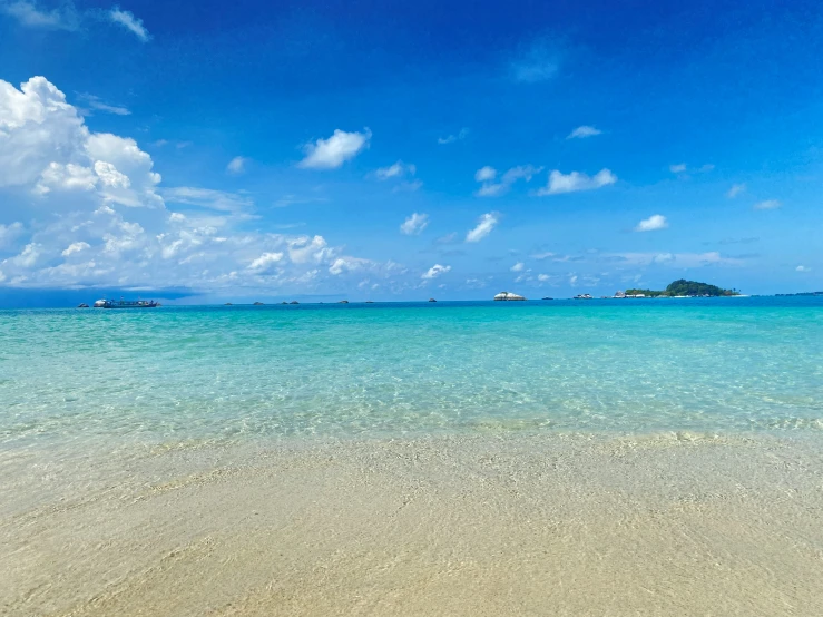 a sandy beach with calm blue water and yachts in the distance