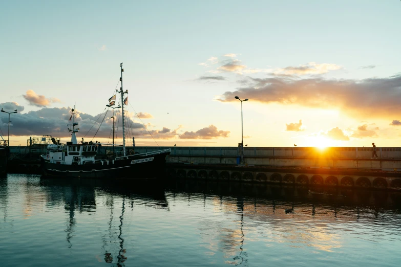 the sun sets over a boat docked at a pier