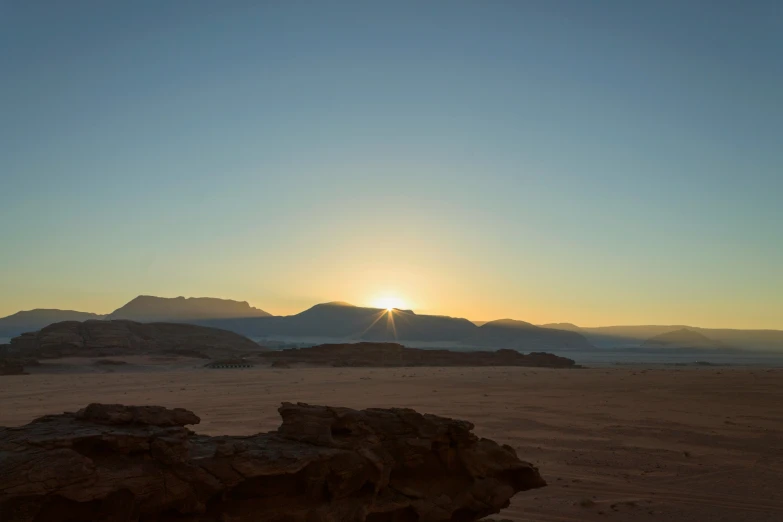 some animals are standing in the sand near mountains