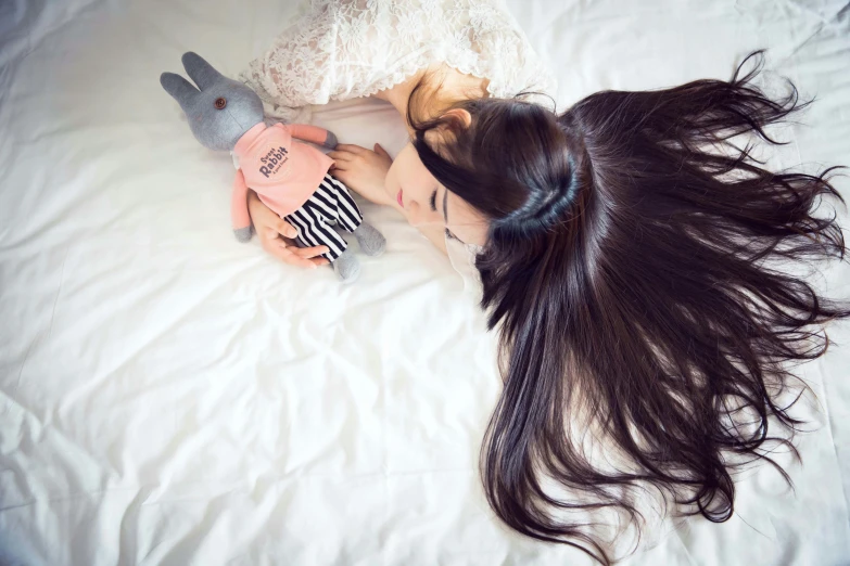 the woman is laying down with her long hair close to a small stuffed bear