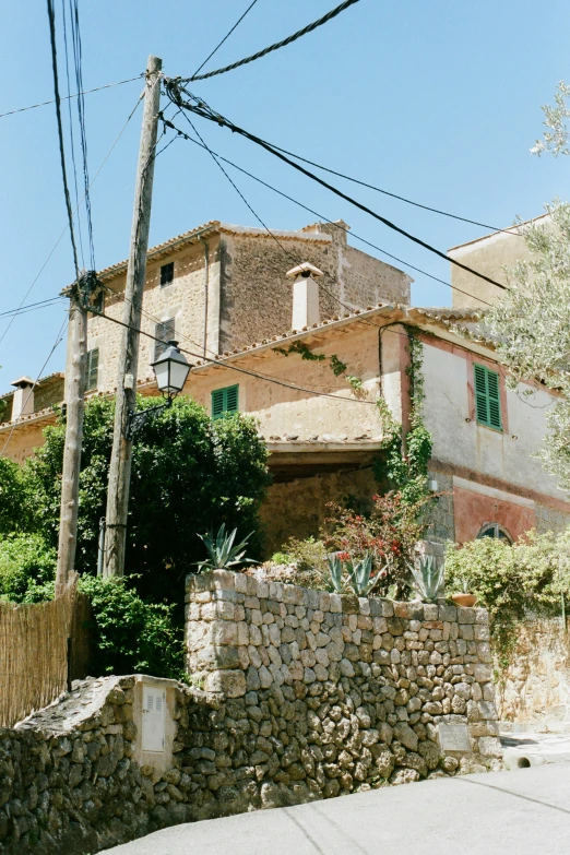 a stone wall next to a house with windows and green shutters