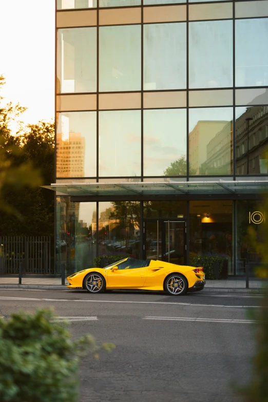 a very nice yellow sports car in front of a glass building