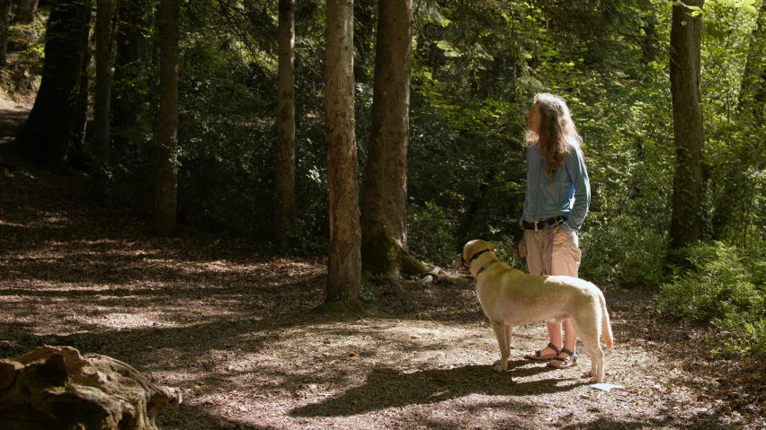 a young lady holds her dog, while looking at the woods