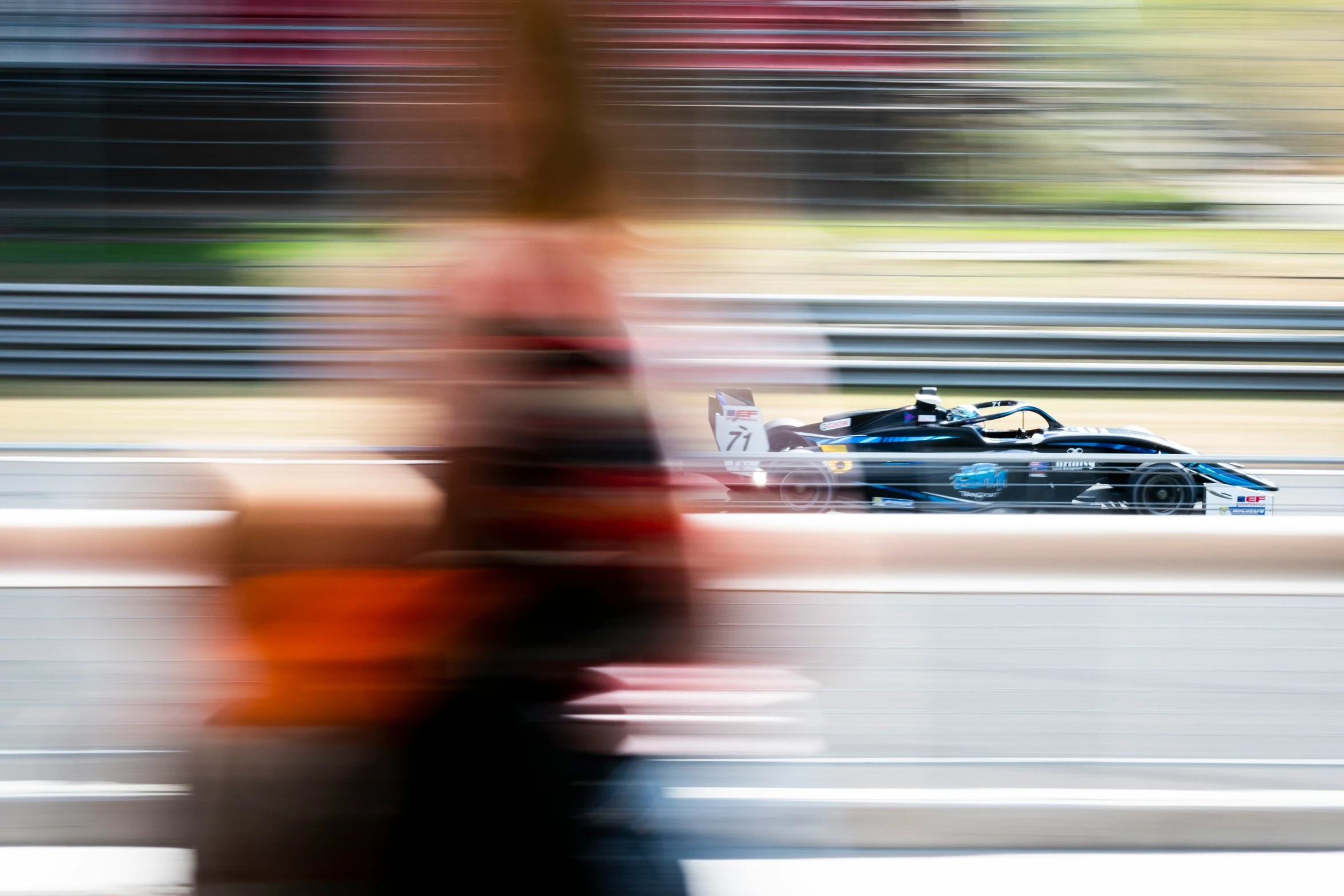 the blurry image shows a person holding up a remote control while standing near a race car