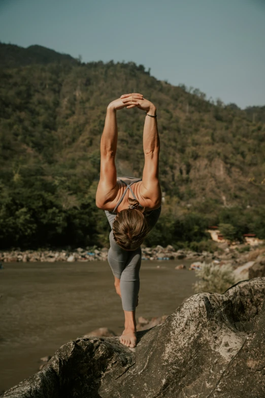 a person doing a hand stand on a rock next to a body of water