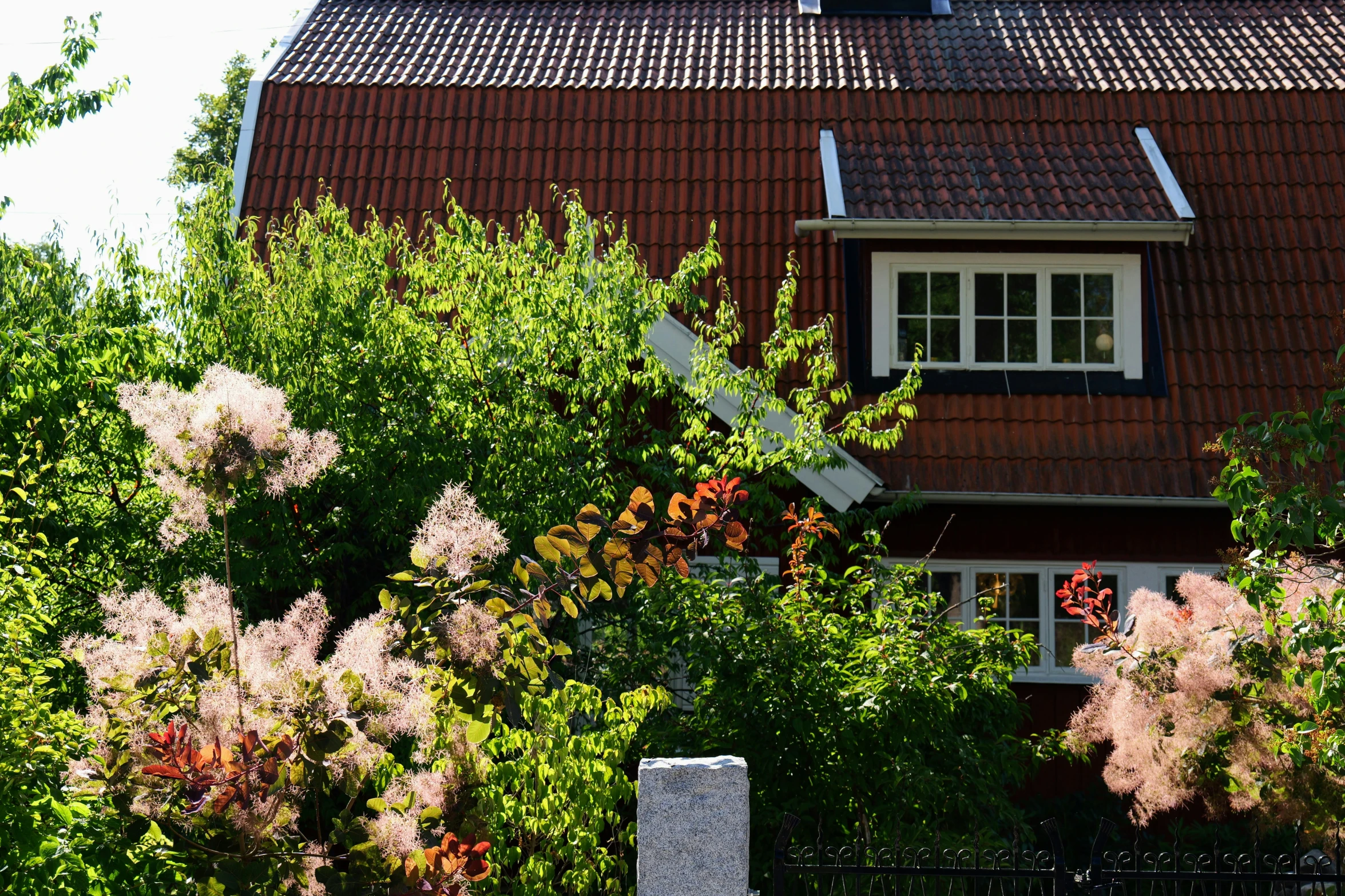 a tall red house with flowers and trees in front