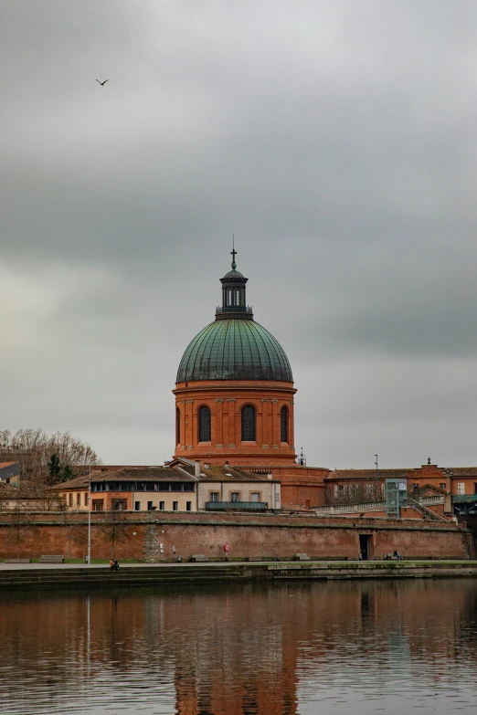 an old brick building and its dome overlooks a body of water