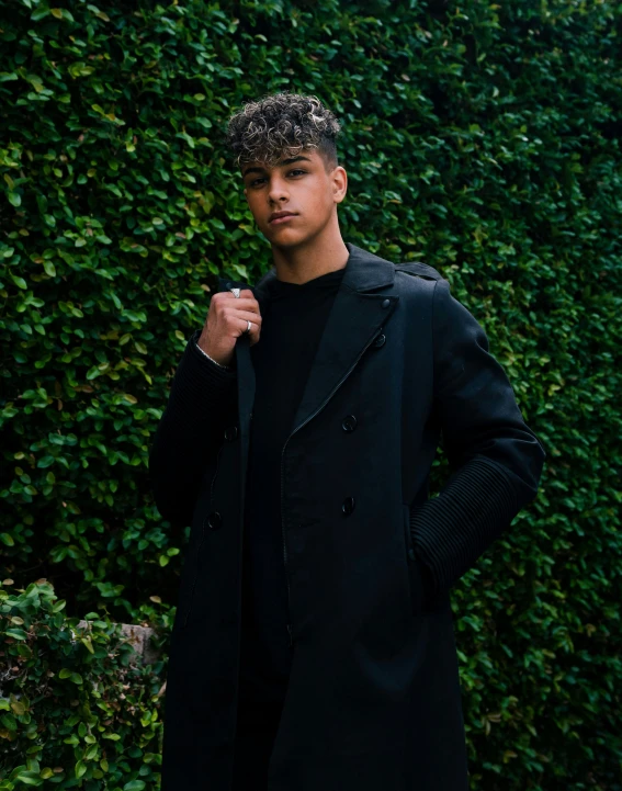 young man with hand in pocket, leaning on ivy covered wall