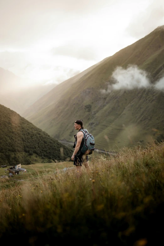 a man wearing backpack standing on grassy area next to mountain