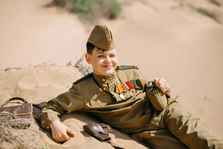 a smiling boy in uniform laying down on sand