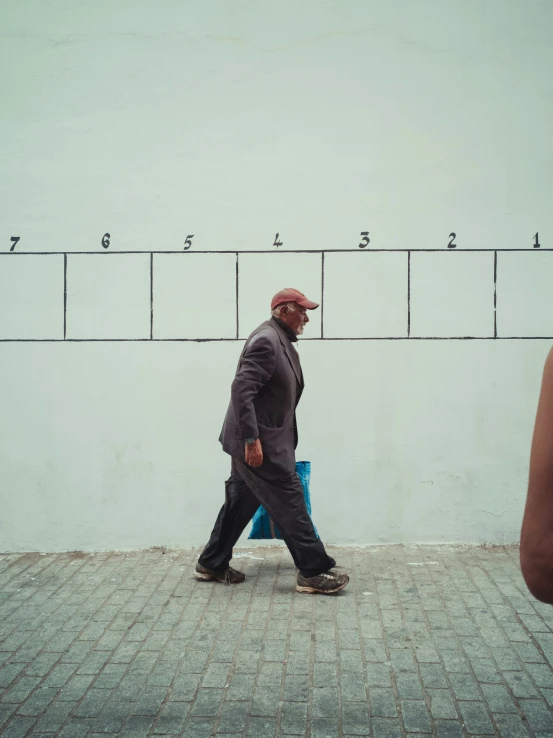 man walking along a sidewalk near a wall with numbers on it