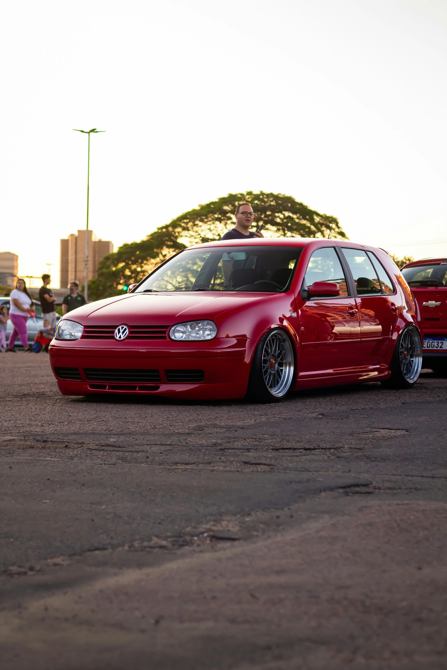 a red car with an odd stance is parked in a parking lot