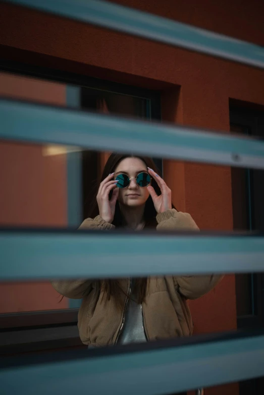 woman looking through blinds with green tinted glasses