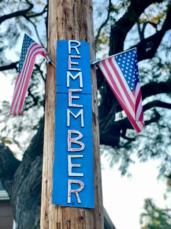 wooden pole with a sign hanging on it with flags hanging off of the side