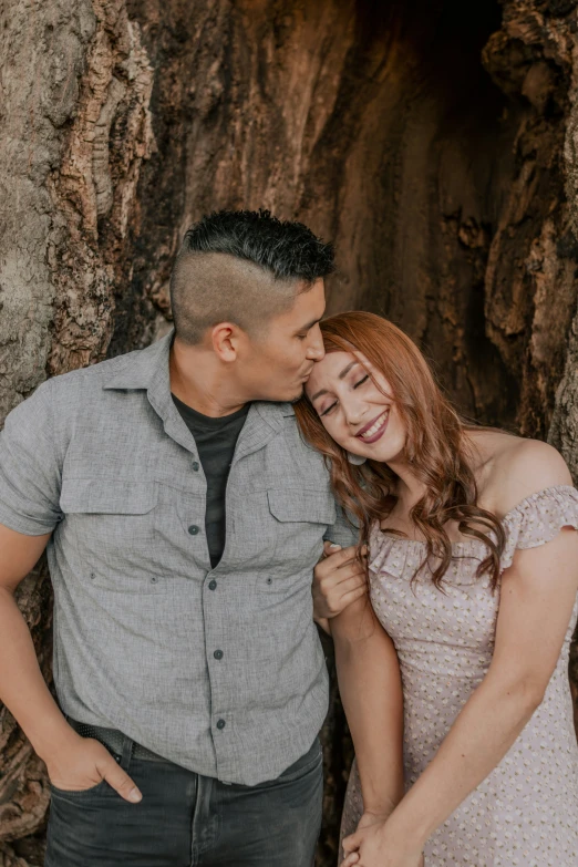 a man and woman in front of a large tree, hugging each other