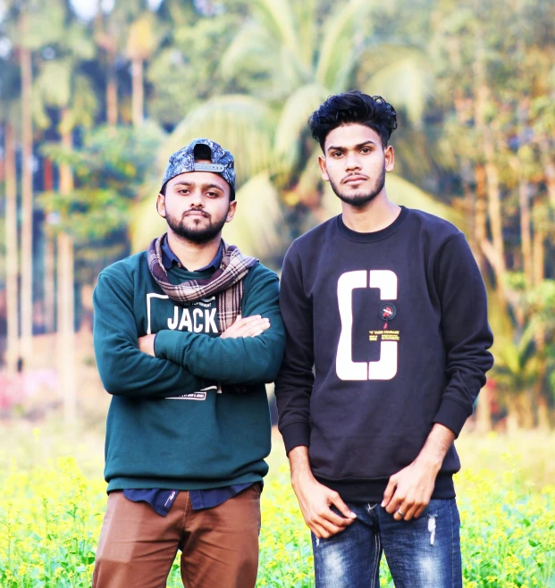 two guys standing in the grass with their arms crossed