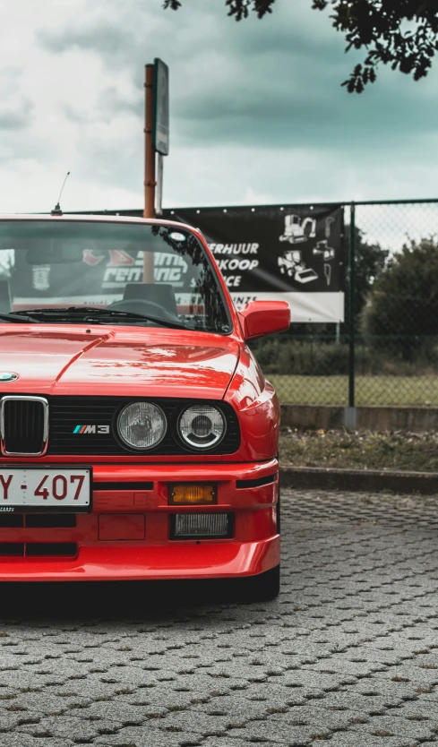 a red bmw car parked next to a metal fence