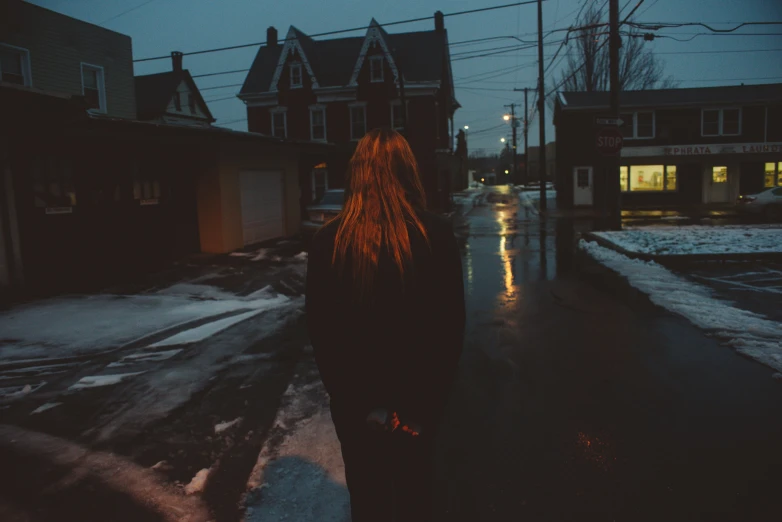 a girl in black is walking down the street at night