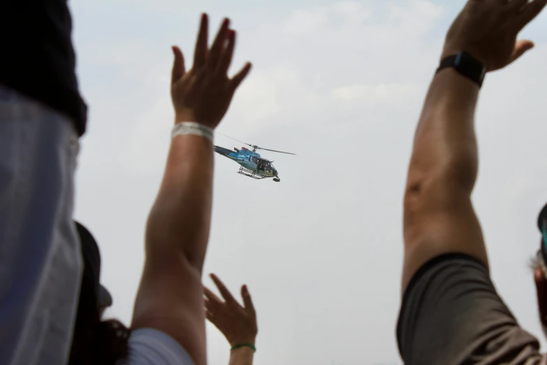 a helicopter flies low above many hands in the air