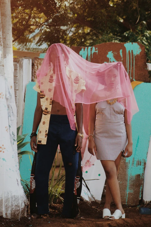 two people standing next to each other with a pink covering over their heads