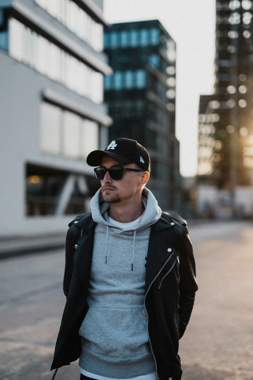 a young man wearing a black hat and sunglasses is standing on the sidewalk