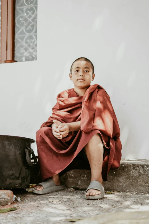 an old man sitting on the ground dressed in a brown robe