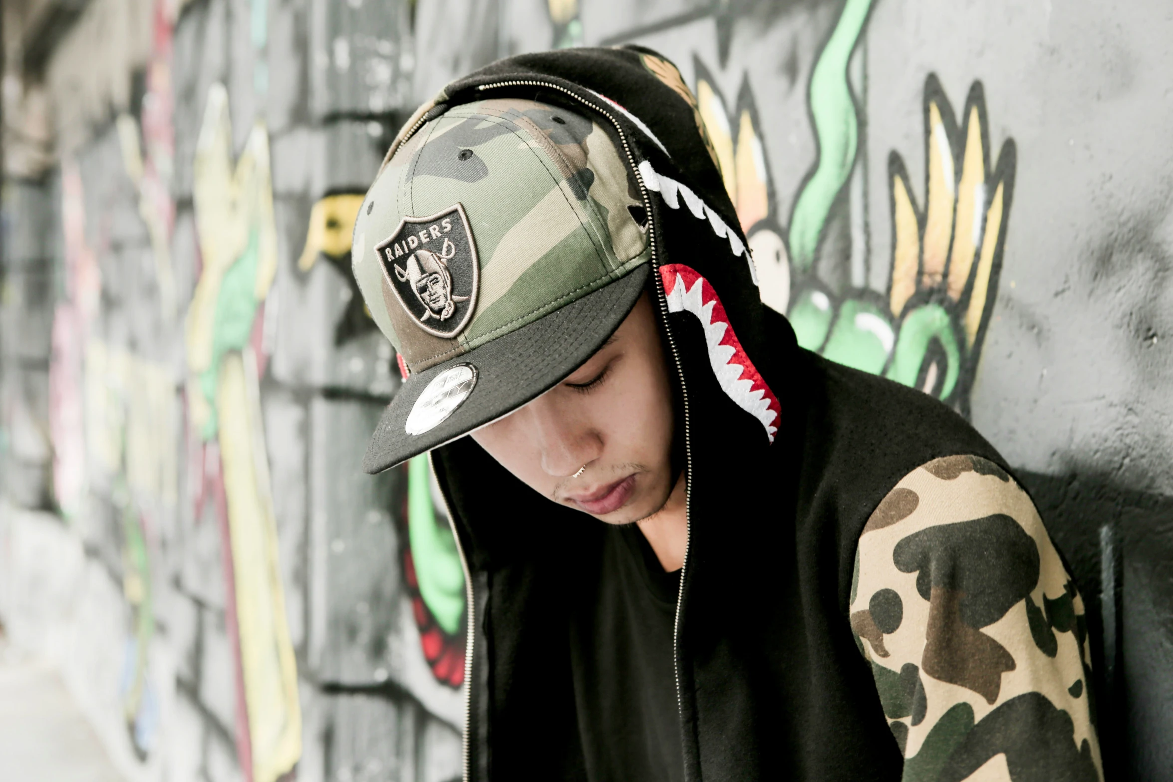 a young man wearing a hat sitting in front of a wall