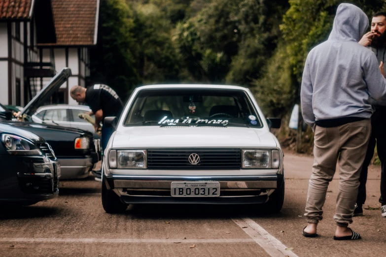 two men stand near two parked cars