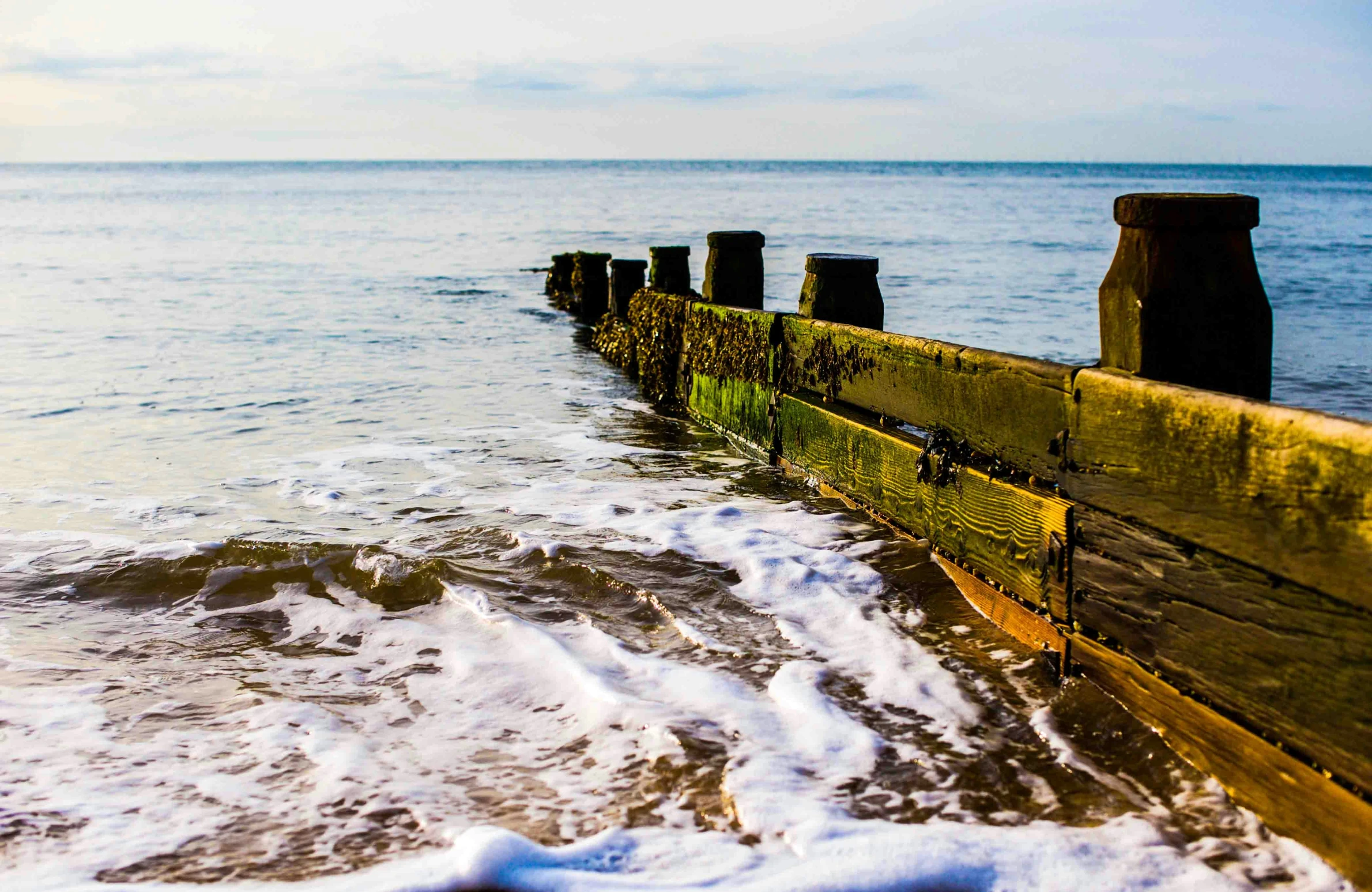 there is water splashing on the beach next to a long wooden railing