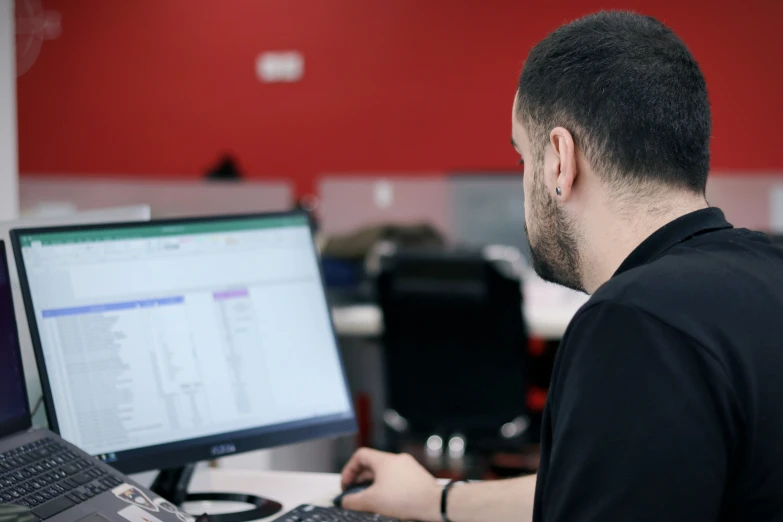 man sitting at computer in front of red wall