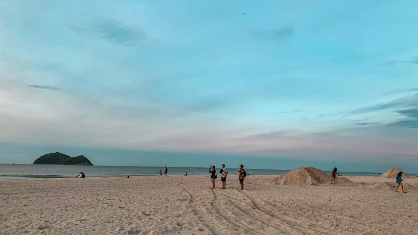 several people walk along a sandy beach near the ocean