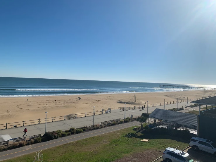 the people are walking on the beach while the cars go by