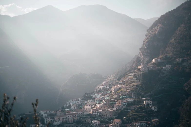 houses nestled in the mountains are shown beneath a misty sky