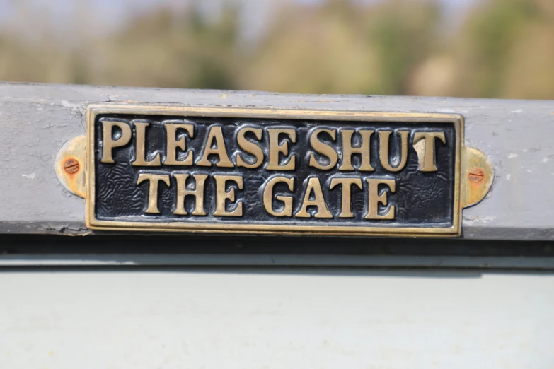 sign saying please shut the gate in black with gold lettering