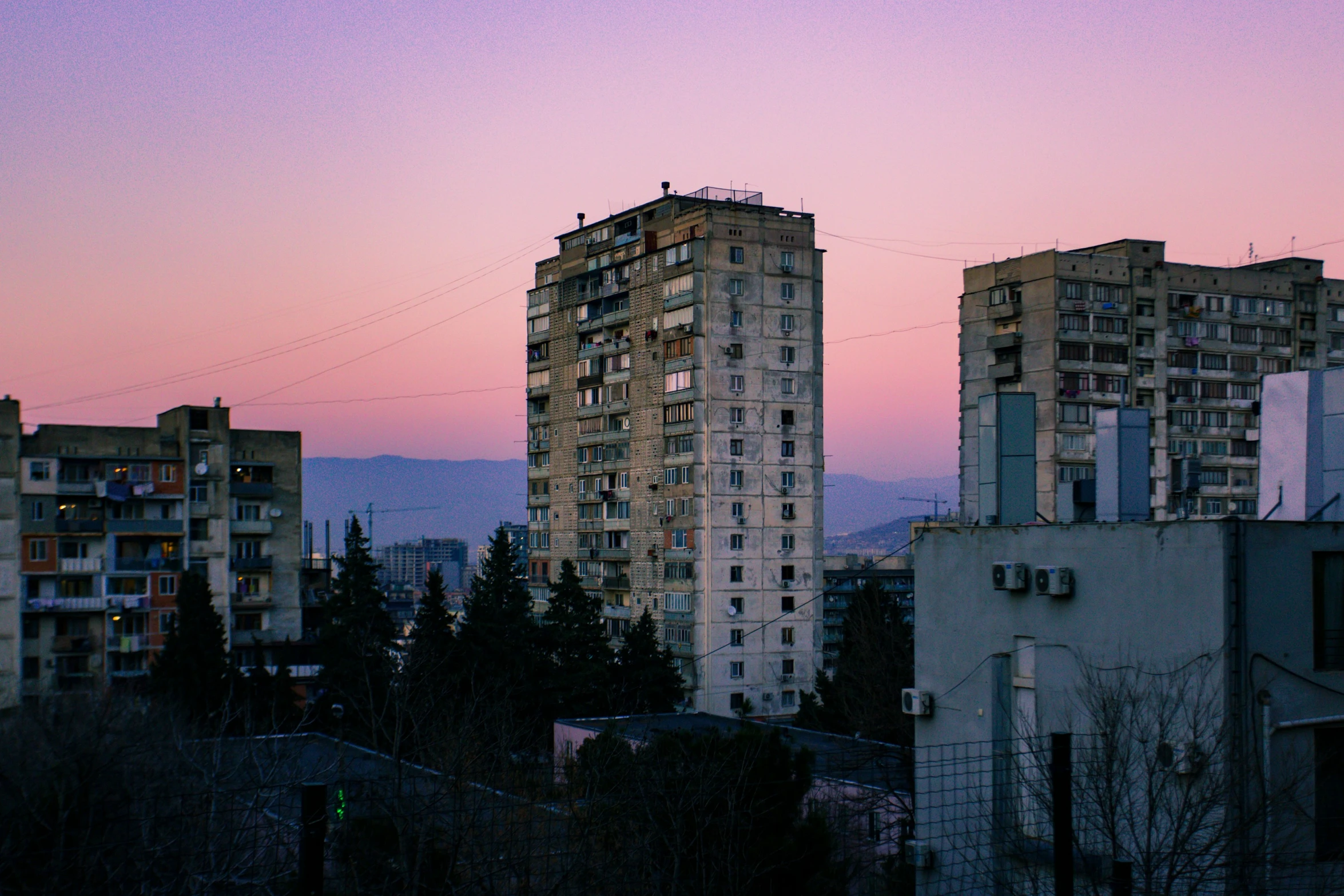 some tall buildings are seen against a colorful sky