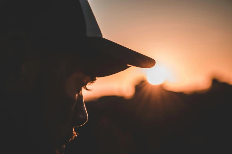 a man wearing a hat and looking at a sunset