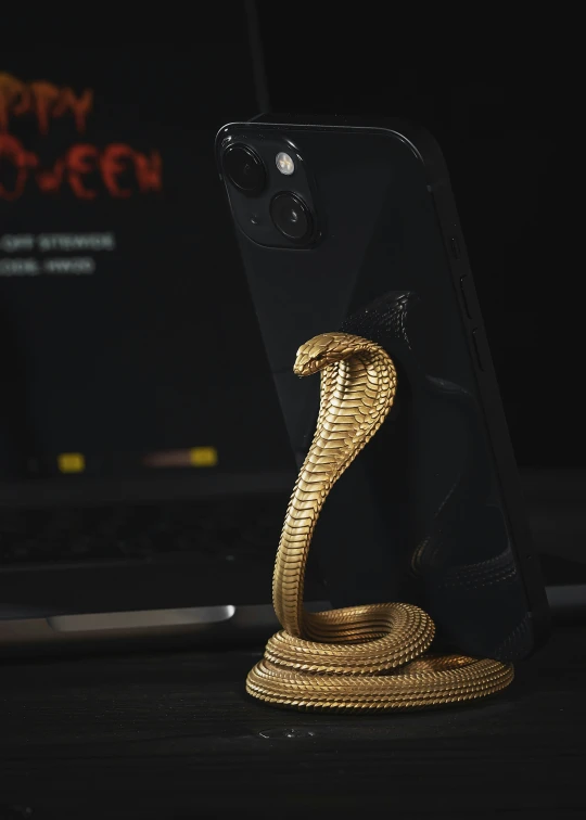a black smartphone sits on top of a golden snake stand