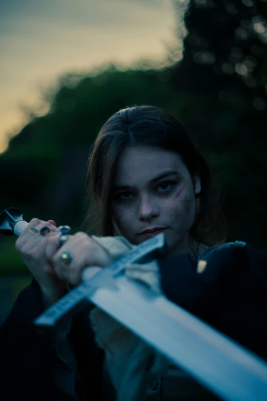 a woman holding a sword in front of a forest