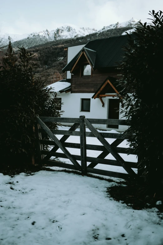 the house has a wooden gate and is surrounded by snow