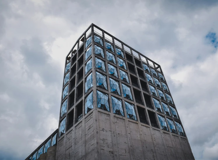 an unusual tower against a cloudy sky and grey clouds