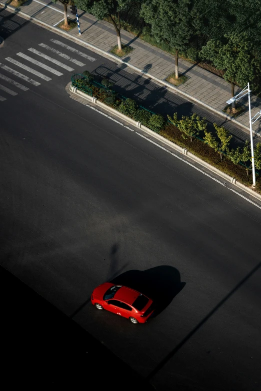 the shadow of an overhead view of a red car on a black road