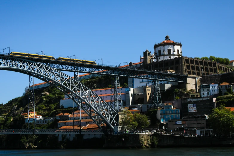 a river boat passing under a bridge on top of a hill